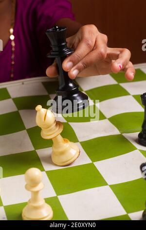 A girl playing chess game. Defeating the White bishop taking the Black Queen in her hand on chessboard. Stock Photo
