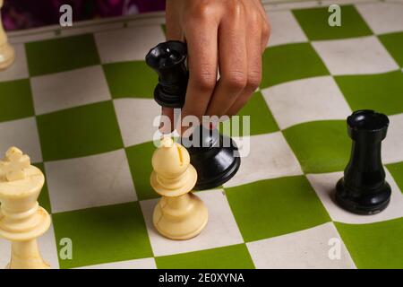 A girl playing chess game. Defeating the White bishop taking the Black Queen in her hand on chessboard. Stock Photo