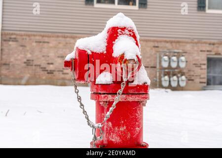 Close up of a bright red fire hydrant against snow and building in winter Stock Photo