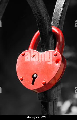 Red lock in the shape of a heart hangs on the railing. Monochrome Background Stock Photo