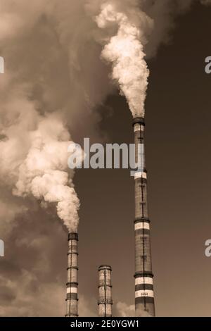 The thick smoke rises high from the industrial pipes. Pollution of the environment with waste products. Black and white photo. Stock Photo