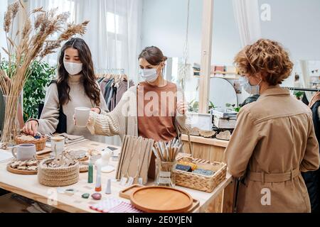 Three young women in ecological shop choosing between various cosmetic products Stock Photo
