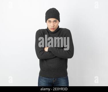 Young handsome asian man wearing grey sweater and beanie hugging herself and trembling, shaking from cold wind, freezing on white background. Stock Photo