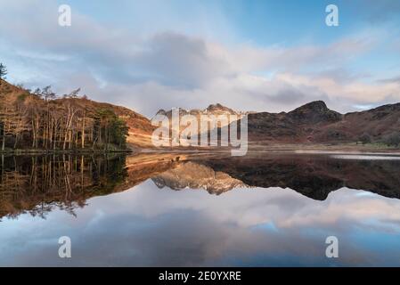 Beautiful Winter sunrise over Blea Tarn in Lake District with snow capped Langdale Pikes in distance Stock Photo