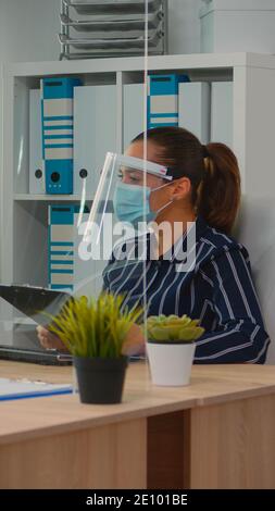 Immobilized freelancer with protection mask in wheelchair having videomeeting during a coronavirus pandemic in new normal business office. Freelancer working in company respecting social distance. Stock Photo