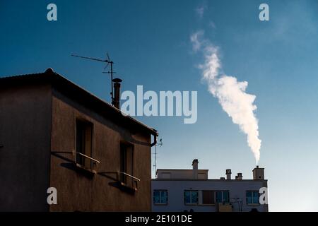 White smoke coming out of a chimney on the roof of a residential building. Concepts of cold, heating, and pollution Stock Photo
