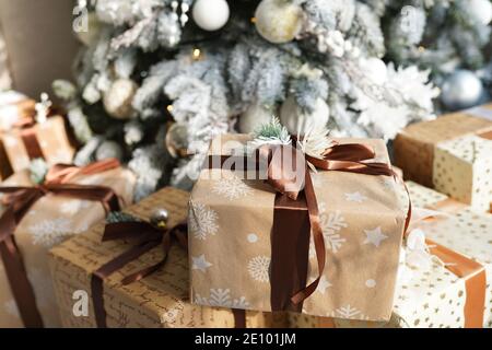 Christmas gift boxes in craft paper with brown ribbons under the fir tree. Stock Photo