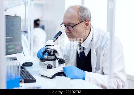 Senior man working in life science laboratory using modern microscope. Chemist researcher in sterile lab doing experiments for medical industry using modern technology. Stock Photo