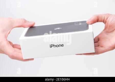 Man and woman hand holding a box with black iPhone 11 on the grey background, December 2020, San Francisco, USA Stock Photo