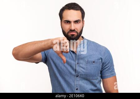 Unhappy dissatisfied man with beard showing thumbs down dislike gesture, symbol of disagree, giving feedback. Indoor studio shot isolated on white bac Stock Photo