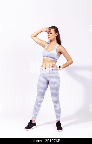 Full length exhausted after workout woman in white sportswear wiping sweat from forehead with hand, confidently looking aside. Indoor studio shot isol Stock Photo