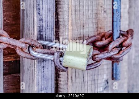 Close up of closed old outdoor bathroom door with padlock and rusty metal chain Stock Photo