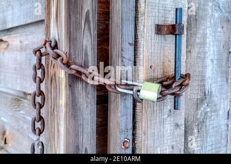 Padlock and rusty metal chain on the wooden door and handle of outdoor bathroom Stock Photo