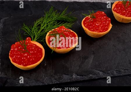 Tartlets with red salmon caviar on black stone plate, decorated with dill and a slice of lemon, close - up. Seafood appetizer Stock Photo