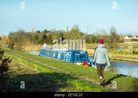 Person walking along the towpath of the Trent and Mersey canal  past a narrowboat moored near Ettiley Heath in Cheshire England Stock Photo