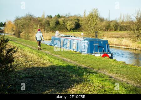 Person walking along the towpath of the Trent and Mersey canal  past a narrowboat moored near Ettiley Heath in Cheshire England Stock Photo