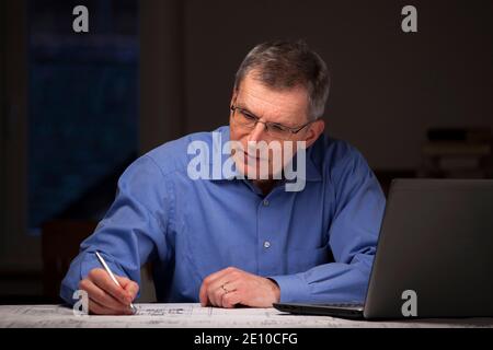 Mature businessman or architect working in a dark room at home - focus on the face Stock Photo