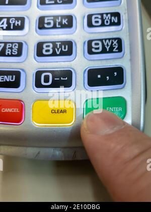 A person using a finger pressing the enter button on a card reader to make a payment. Stock Photo