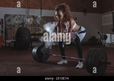 Beautiful female crossfit athlete preparing for deadlift exercise, chalking her hands. Attractive athletic woman using magnesium before working out wi Stock Photo