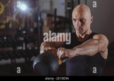 Mature athletic man working out with kettlebell at crossfit box gym. Concentrated muscular sportsman doing kettlebell swings, copy space. Crossfit, st Stock Photo