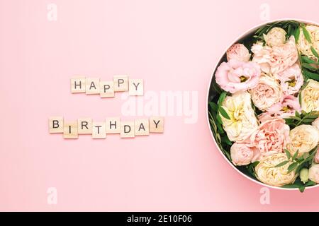 Happy birthday lettering on the wooden squares with letters on the pink background and big round box with red flowers and roses. Greeting card concept Stock Photo