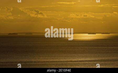 View from Emmettes Hill in Dorset along the Jurassic coast towards ships anchored in front of Portland Harbour as the sun starts to set behind them. Stock Photo