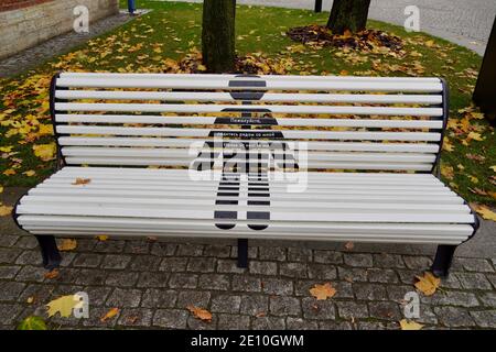 Empty grey bench in the park against the background of autumn leaves Sign Please sit next to me, Pandemic time, Amazing man is drawing on the bench