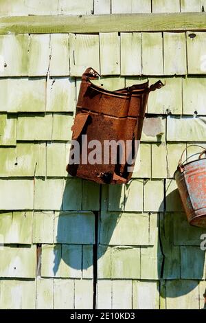 Rusted Bucket with Large Holes Hanging from Green Wall in Sunlight Stock Photo