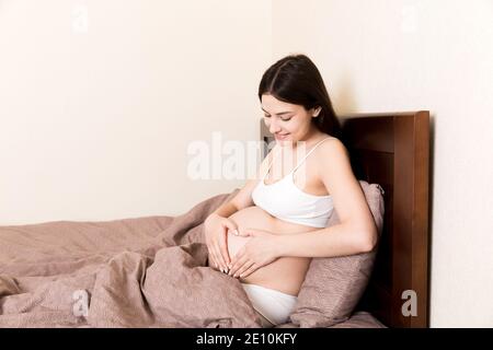 happy pregnant woman making heart in home on bed. Pregnancy, love and expectation concept. Stock Photo