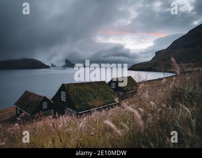 Bour village Grass-covered picturesque houses at the Faroese coastline in the village Bour with view onto Dranganir and Tindholmur during spring. Stock Photo