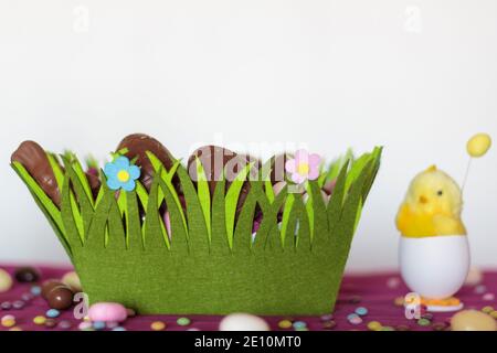 Easter basket with chocolate eggs, decorative chick and almonds on table against white background Stock Photo