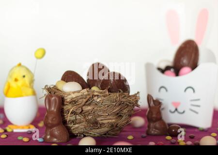 Easter holiday sweetson table. Nest with chocolate eggs, chocolate rabbits, treat box with easter eggs and decorative chick Stock Photo