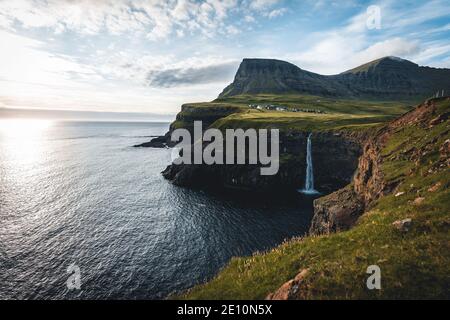 Gasadalur village and Mulafossur its iconic waterfall during summer with bluw sky. Vagar, Faroe Islands, Denmark. Rough see in the north atlantic