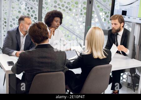 Business, teamwork concept. Group of focused professional international partners, discussing details of joint project in modern meeting room Stock Photo