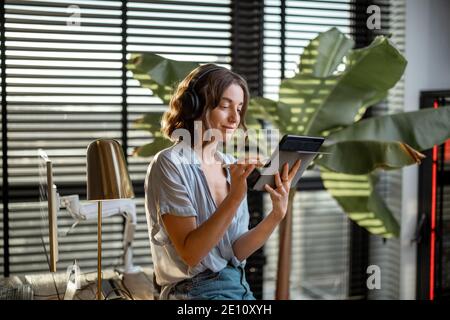 Young woman works on a touchpad, feeling comfortable at cozy home office with a green plant on the background Stock Photo
