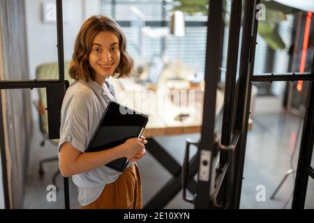 Portrait of a young cheerful woman standing with a digital tablet at the cozy and stylish home office Stock Photo