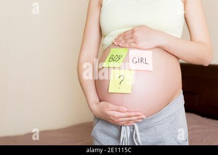 pregnant woman holding square multicolored stickers with question marks. Stock Photo