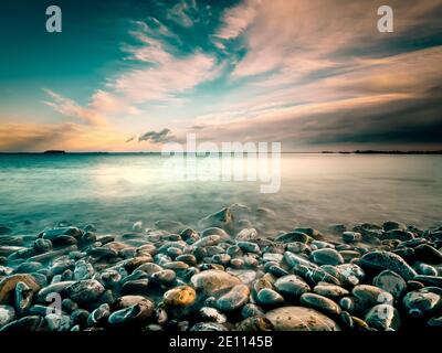 Coastline With Pebbles And Motion Blurred Ocean During Evening Stock Photo