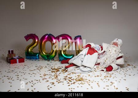 Santa Claus celebrating xmas and 2021 new year laying on floor with gifts, balloons and confetti Stock Photo