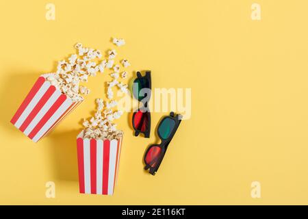 Popcorn in a red striped buckets and 3d colourful glasses top view on yellow background. Cinema concept. Stock Photo