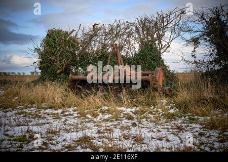 Old Howard agricultural PTO driven rotovator abandoned at the edge of a  field by a hedgerow in the snow Stock Photo