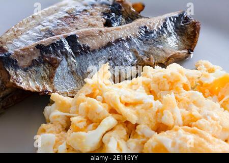 Kippers with scrambled eggs served on a white plate. A kipper is a whole herring, a small, oily fish. Kippers are one of the types of fish high in Ome Stock Photo