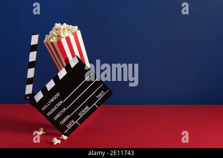 Popcorn in a red striped bucket and cinema clapperboard on red and blue background. Cinema concept. Stock Photo