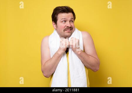 Scared young sporty man with towel looking aside. Studio shot on yellow wall. Stock Photo