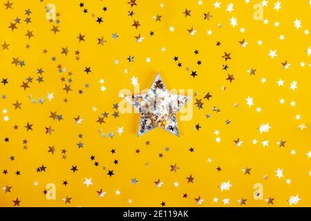 Big star shape with sparling golden and silver stars among star shape glittering confetti on the yellow background. Festive concept. Be unique, to Stock Photo