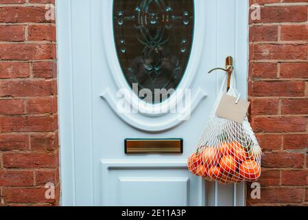 Reusable string bag from environmentally friendly materials with citrus fruits and blank card hanging on the door handle. Local farmer healthy food Stock Photo