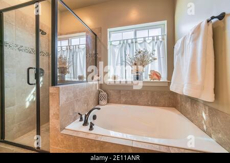 Bathtub and shower stall of warm toned bathroom with tiled wall and floor Stock Photo