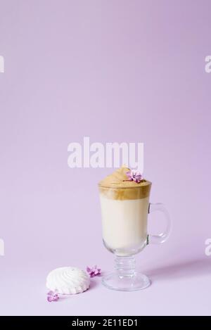 Beautiful dalgona drink a frothy coffee in a transparent mug and flowers lilac to purple Il purple background. Next to the mug is a marshmallow. Copy Stock Photo