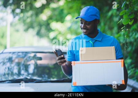 African postal delivery courier man using smart phone and delivering package Stock Photo