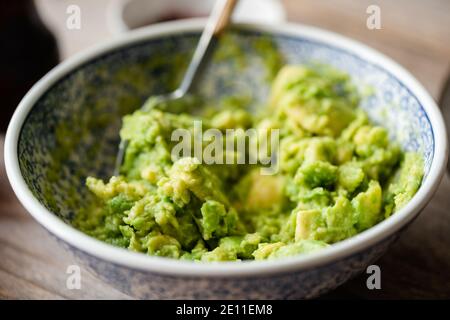 Mashed avocado, guacamole sauce in a bowl, closeup view. Healthy vegan food Stock Photo